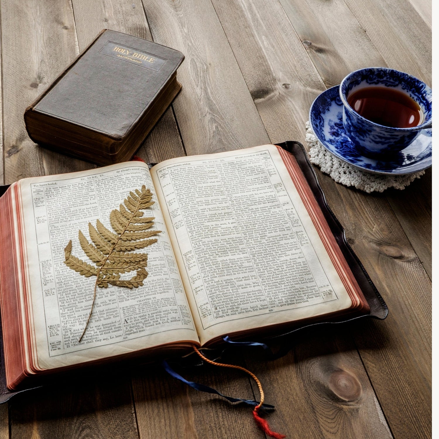 Open Bible with a golden leaf bookmark on a wooden table beside a blue teacup, symbolizing peace, prayer, and reflection. Faith & Inspiration Collection by Perfectly Balanced Beauty – where faith meets elegance and daily devotion begins.