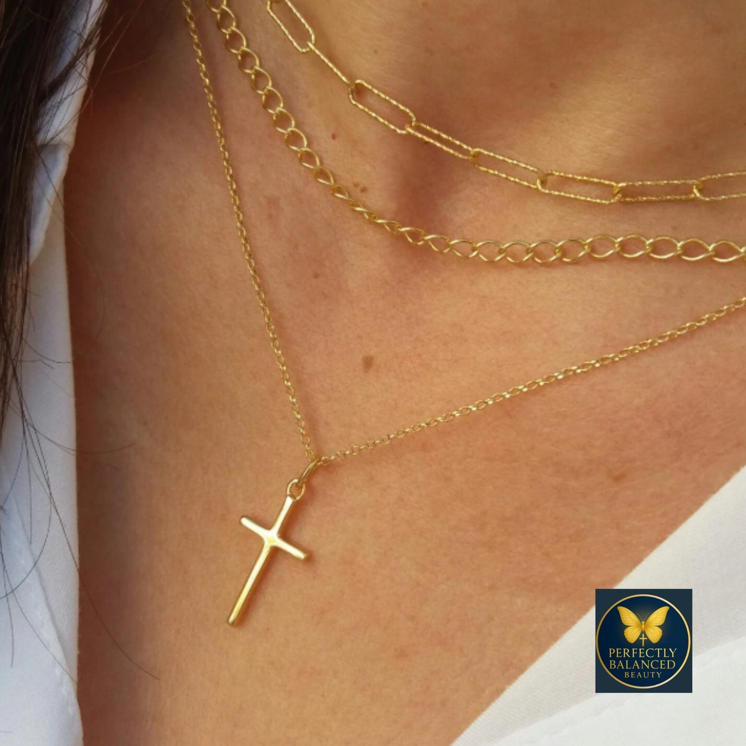 Layered gold necklaces featuring a cross pendant and a decorative eye-shaped pendant on a neutral blouse — fashion jewelry highlighting layered elegance and detail.