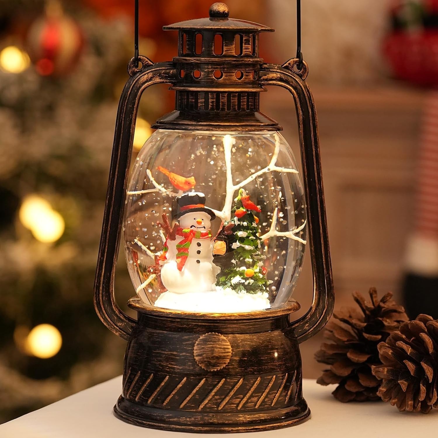 Vintage bronze lantern with a snowman, Christmas tree, and falling snow inside, displayed in a warm holiday setting with soft lights and a pinecone nearby.